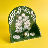 A decorative ceramic wall shelf with a small cup placed on it. Both feature an oak and acorn motif in a hunter green colour with gold accents.
