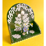 Decorative ceramic wall shelf featuring a motif of oak leaves and acorns with gold embellishments. There's a small cup placed on the shelf with tiny flowers in it.