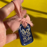 short rectangular ceramic tile ornament decorated with a deep blue crackled glaze and a handpainted ribbon in gold.