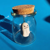 A grumpy ceramic ghost figurine suspended in a glass jar. 