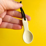A hand holding a small ceramic spoon decorated with a very pale green matte glaze.