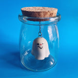A skeptical ceramic ghost figurine suspended in a glass jar. 