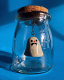 An anxious ceramic ghost figurine suspended in a glass jar. 