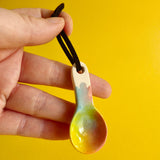 A hand holding a small ceramic spoon decorated with blurred rainbow colours.