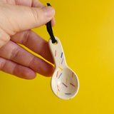 A hand holding a very small ceramic spoon decorated with colourful vertical lines that resemble sprinkles.