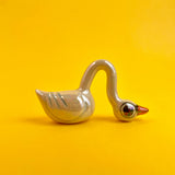 A small ceramic swan figurine with an exaggeratedly long neck resting its silly head on the ground. 