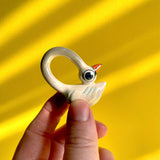 A white ceramic swan figurine with an exaggeratedly long neck resting its head on its own back making a loop.