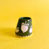 A very small ceramic cup painted green and decorated with white stylized acorns.