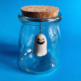 A smiling ceramic ghost figurine suspended in a glass jar. 