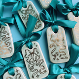 rectangular ceramic tile ornaments with an aqua crackled glaze and gold painted ribbons. Topped with turquoise satiny ribbons